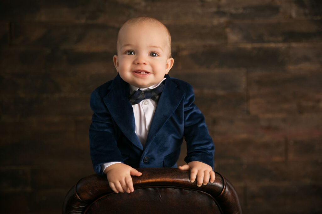 One year old boy smiling in a blue velvet suit during a formal portrait session