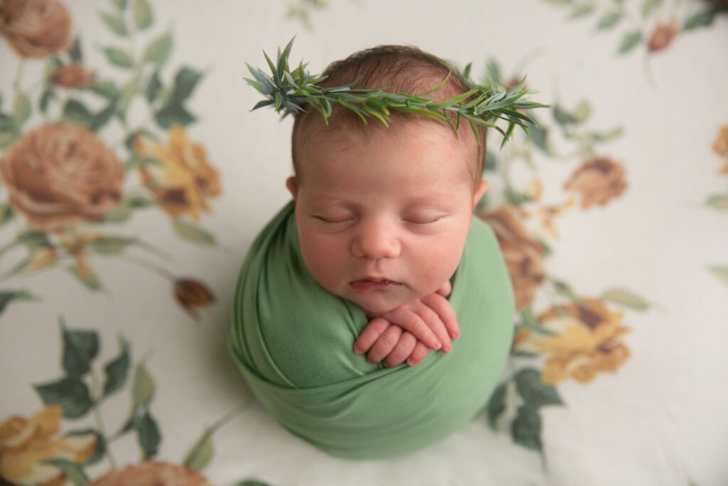 Sleeping newborn wrapped in green fabric with a greenery crown during a newborn portrait session
