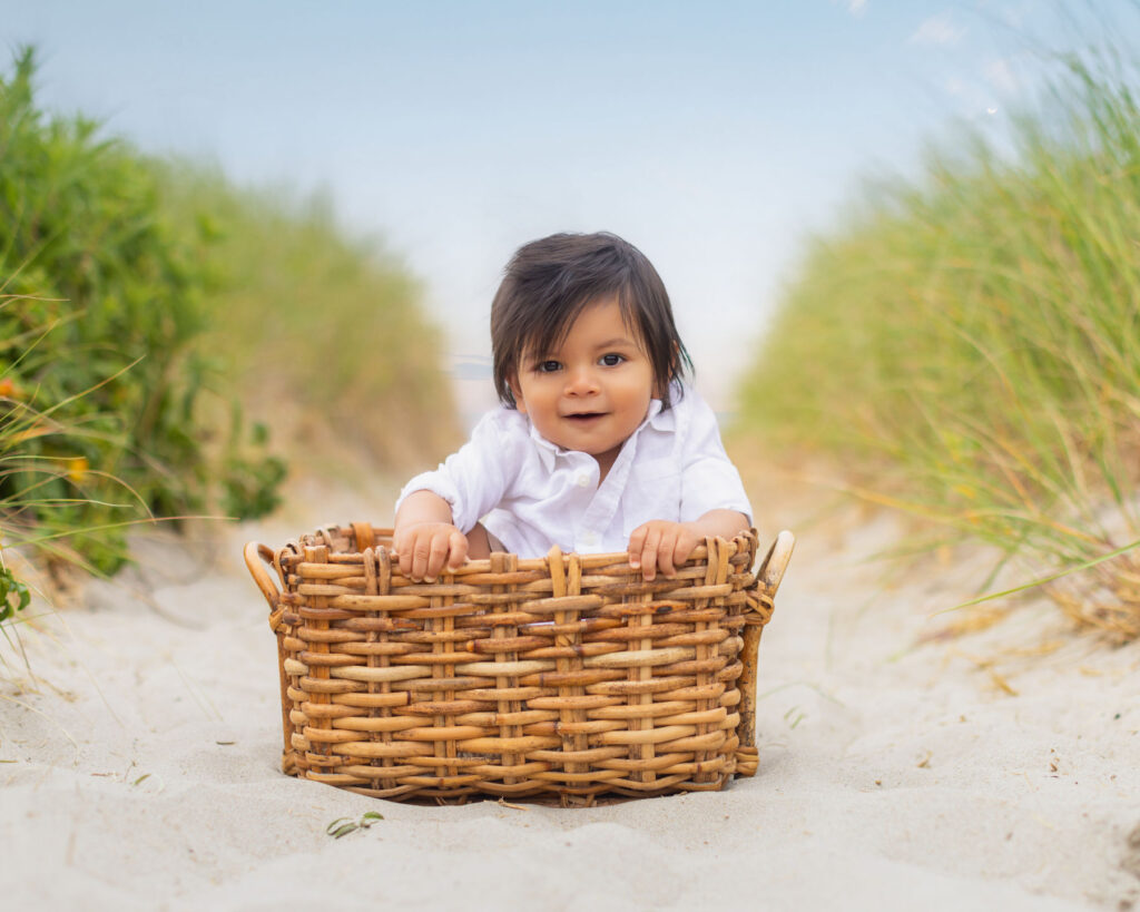 Toddler sitting in basket on sandy beach during portrait session.