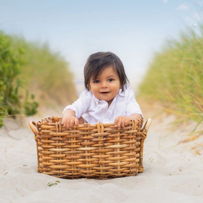 Toddler sitting in basket on sandy beach during portrait session.