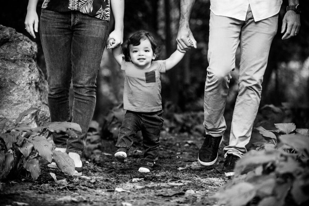 Toddler walking hand in hand with parents during outdoor family portrait session.