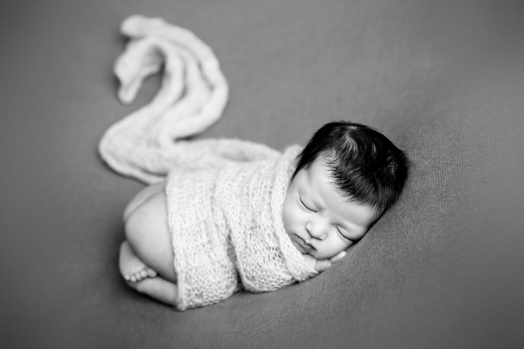 Black and white portrait of sleeping newborn baby wrapped in soft knit fabric