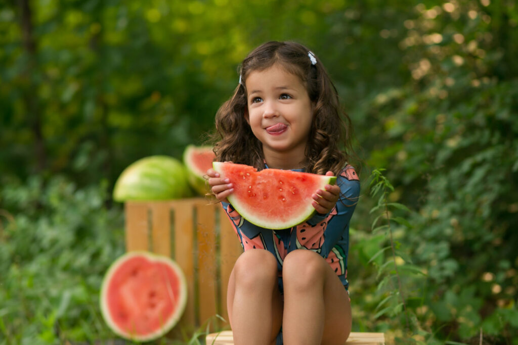 Young girl enjoying a watermelon slice during a playful outdoor child photography session near Boston MA