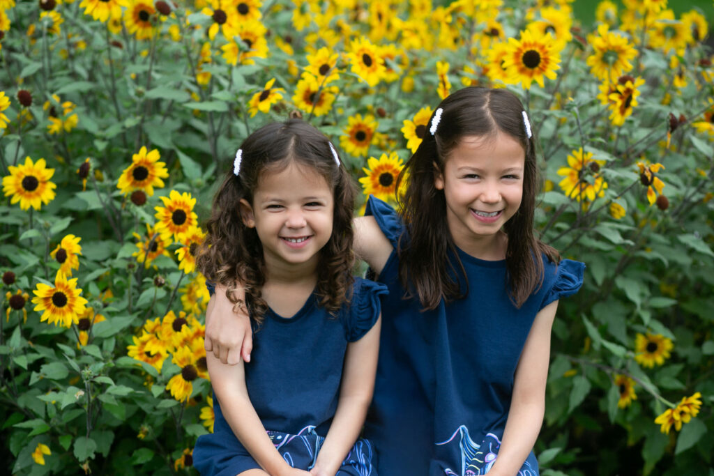 Two sisters smiling together in sunflower field.