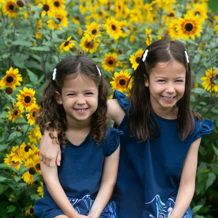 Two sisters smiling together in sunflower field.