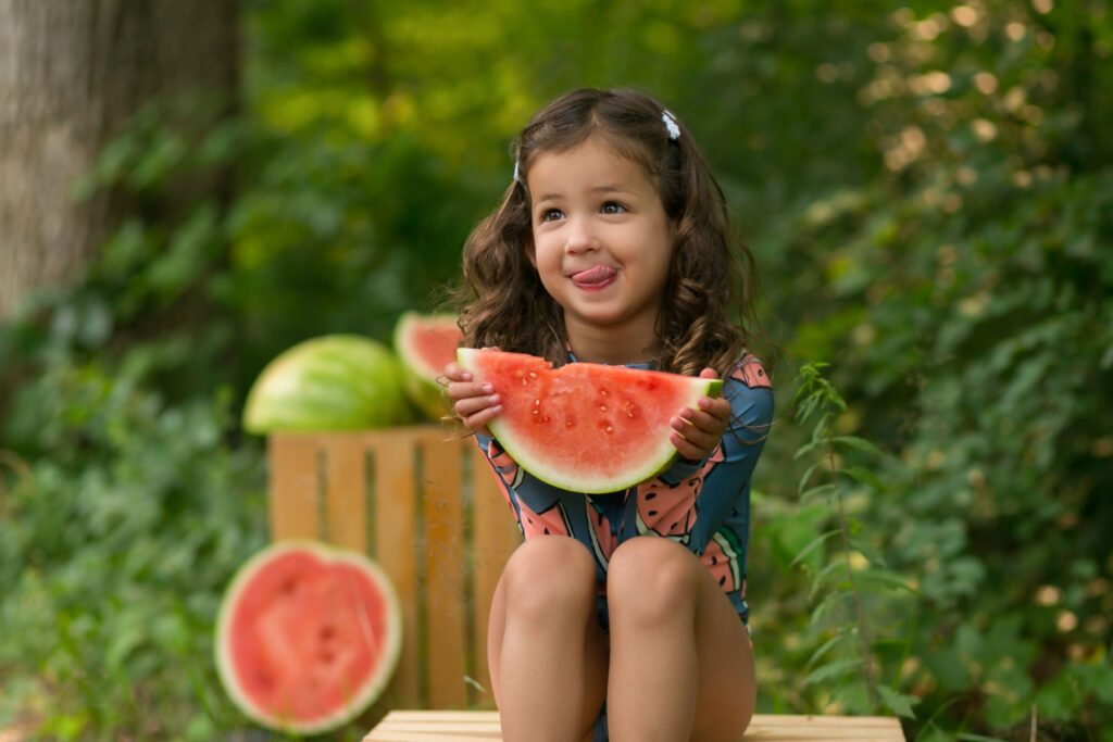 Young girl enjoying watermelon during an outdoor summer children's photography session.