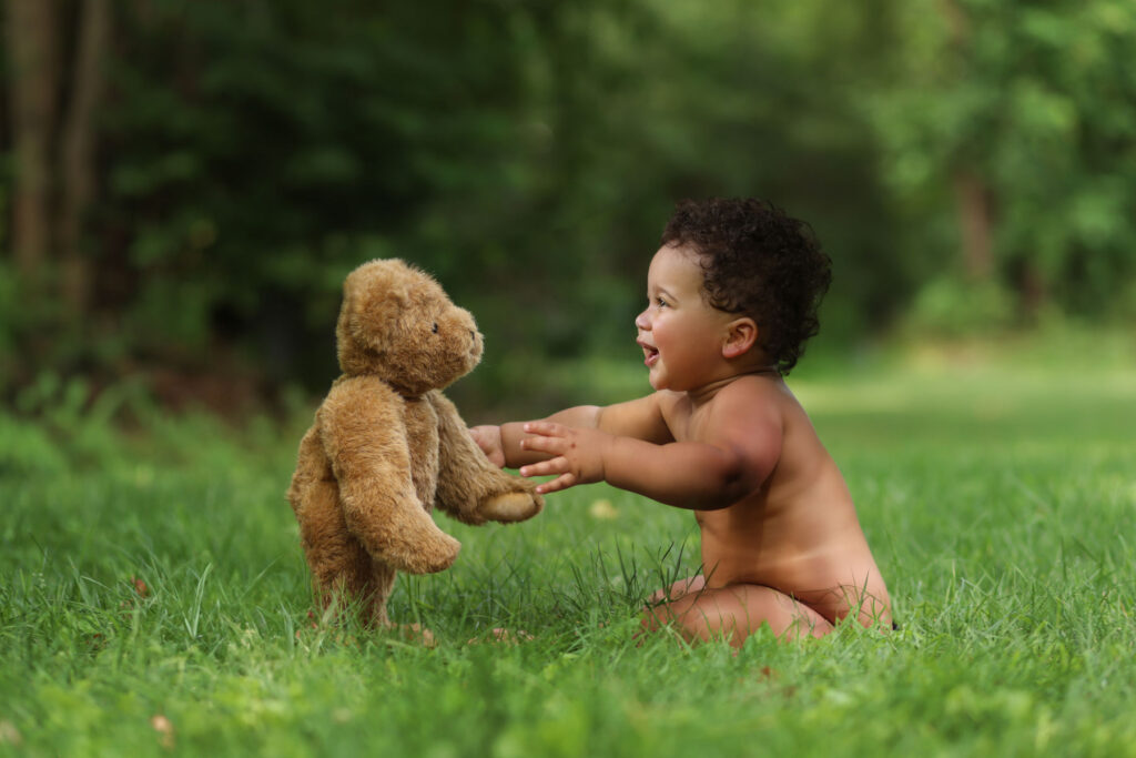 Smiling child interacting with a teddy bear during an outdoor portrait session