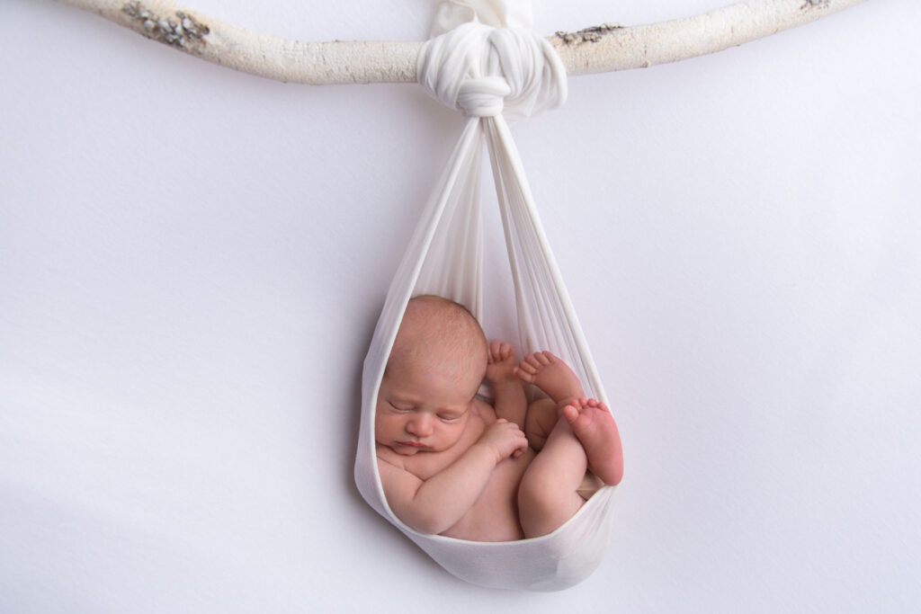 Sleeping newborn posed in soft white fabric during a creative studio newborn session