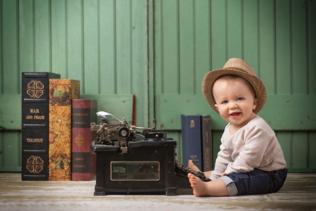 Smiling baby sitting beside a vintage typewriter during a creative milestone portrait session
