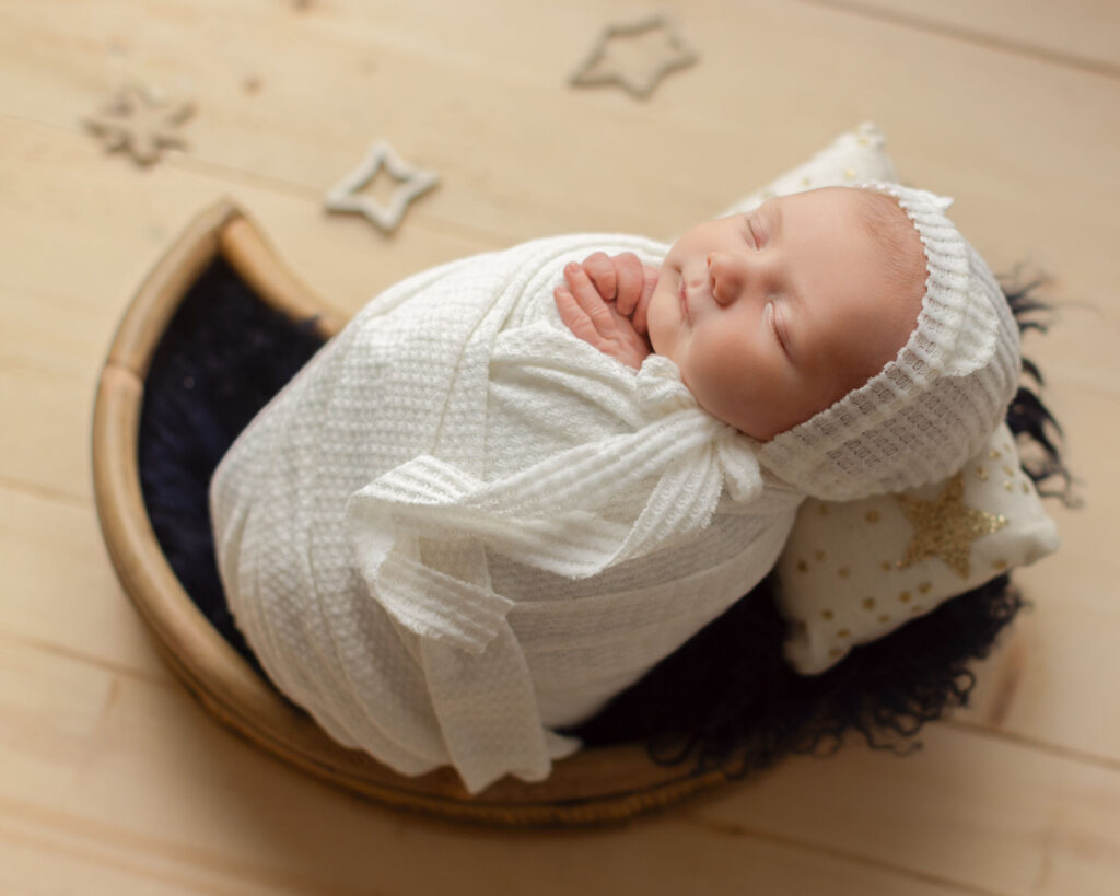 Sleeping newborn wrapped in white during a moon and stars themed studio portrait