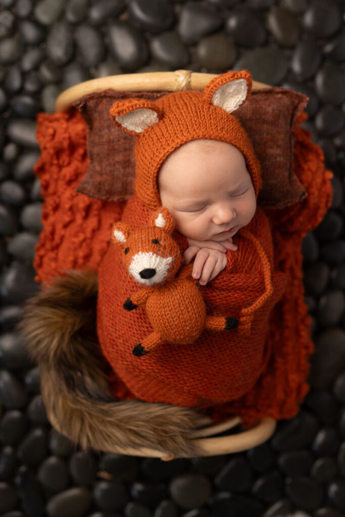 Sleeping newborn in a fox-themed setup with warm rust colors and soft textures