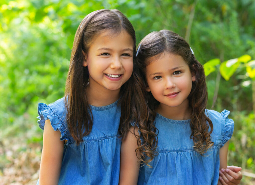 Two smiling young sisters wearing matching blue dresses during an outdoor child portrait session