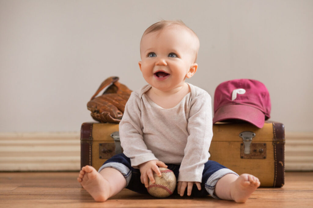 Smiling baby holding a baseball with baseball-themed props during a milestone session