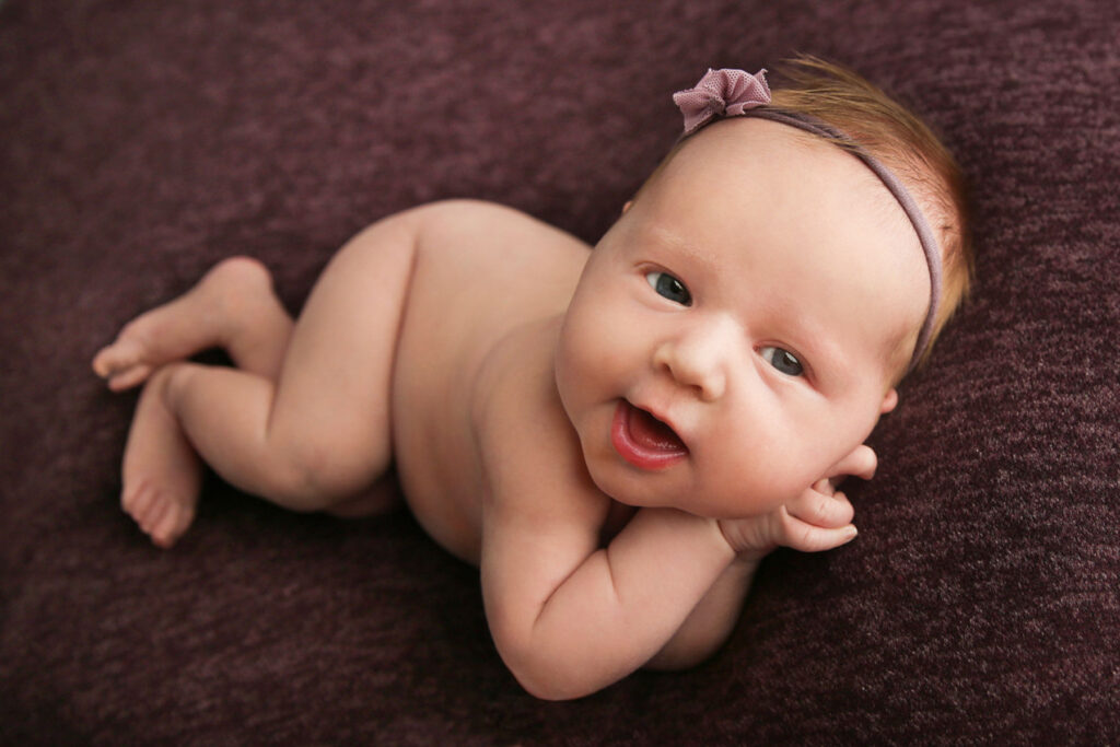 Awake newborn smiling during a studio portrait session with a plum-colored backdrop