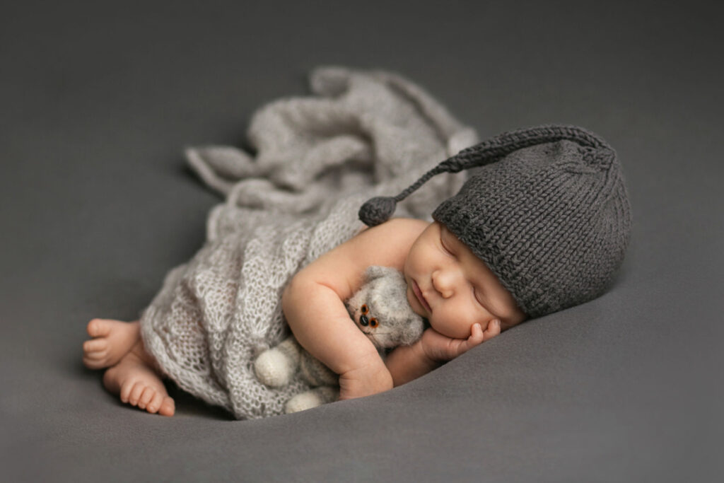 Sleeping newborn wearing a gray knit cap and wrapped in soft fabric during a studio newborn session