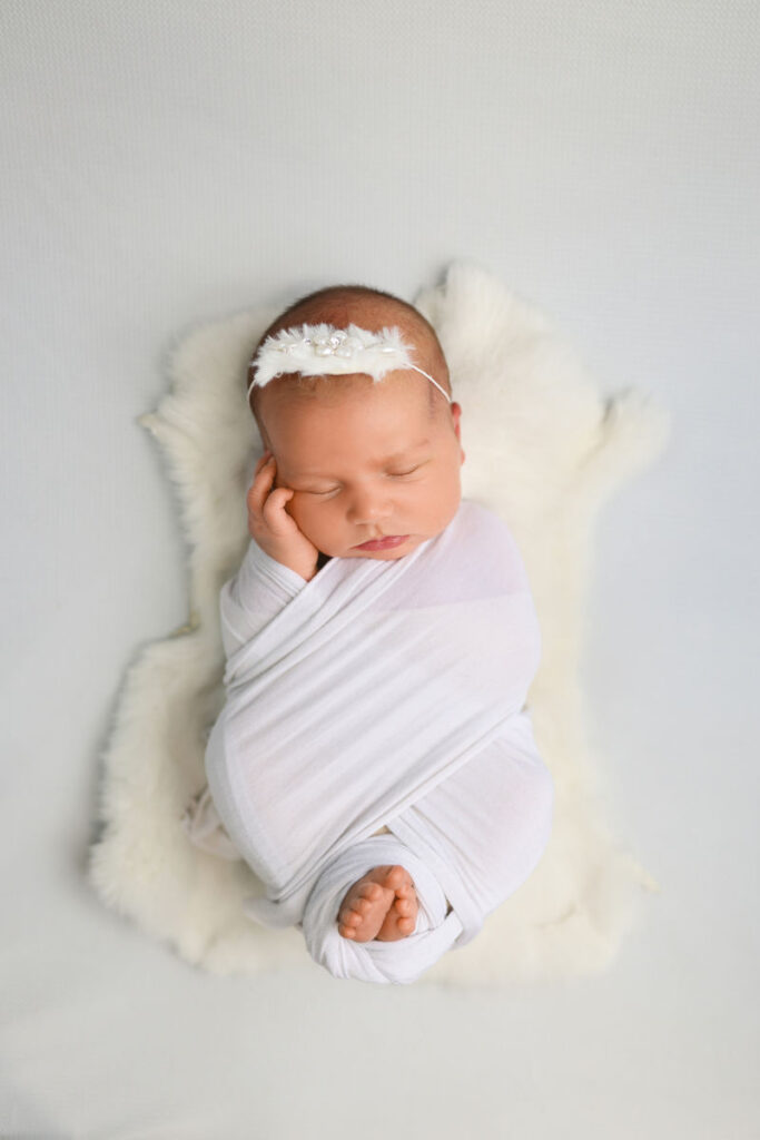 Sleeping newborn wrapped in white with a delicate headband during a studio newborn session