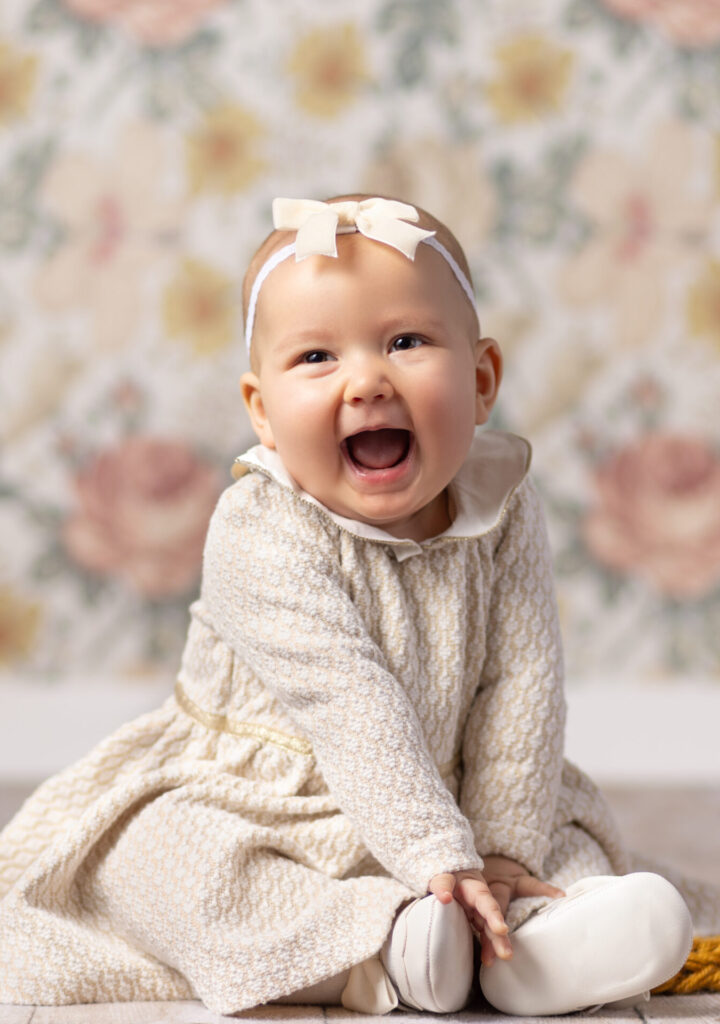 Smiling baby girl in a cream dress during a sitting milestone photography session in Norwood, MA