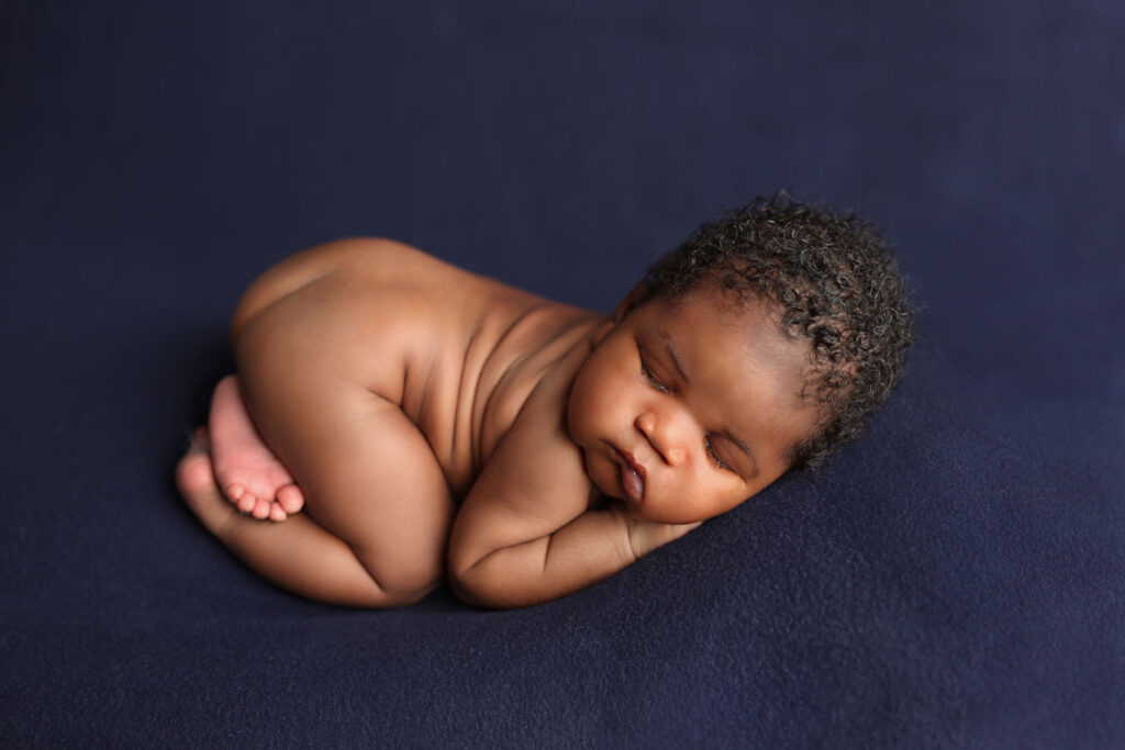 Sleeping newborn baby boy in a curled-up pose during a professional newborn photography session in Norwood, MA