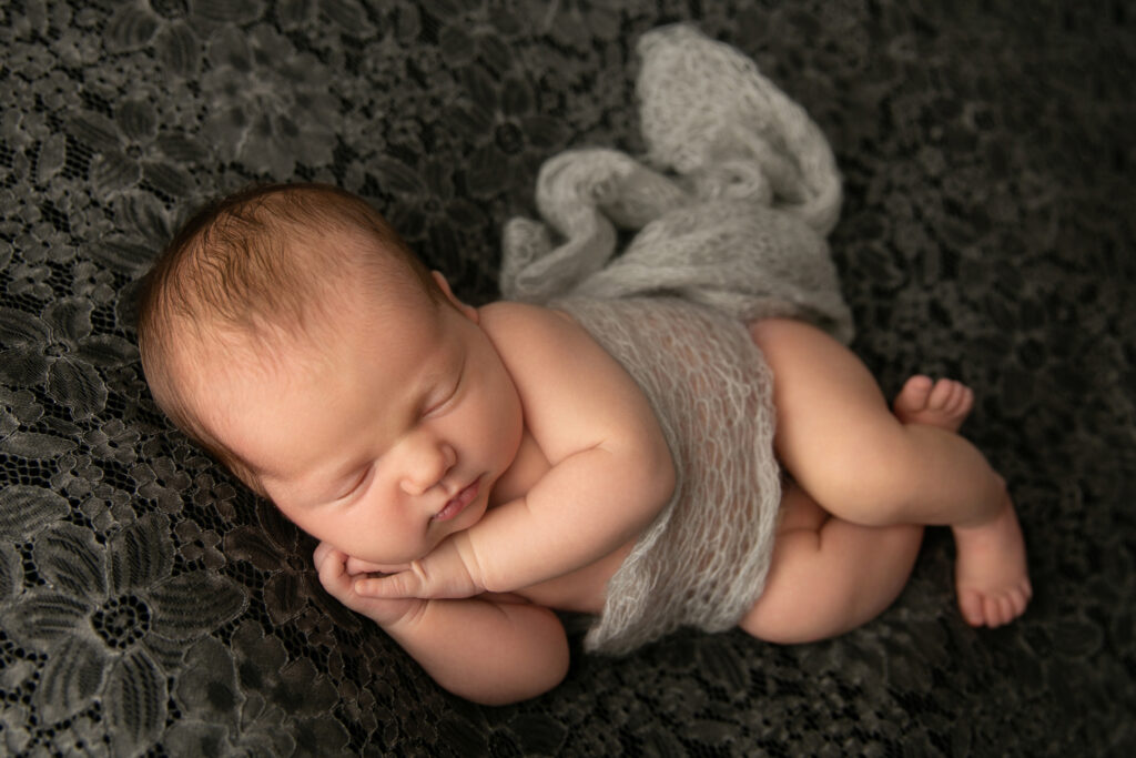 Sleeping newborn baby posed on dark grey lace fabric during a professional newborn photography session