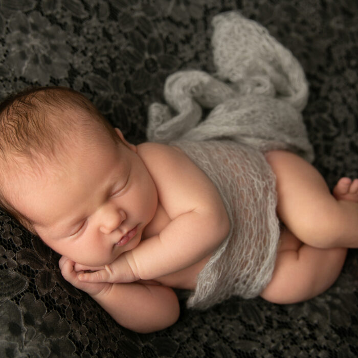 Sleeping newborn baby posed on dark grey lace fabric during a professional newborn photography session