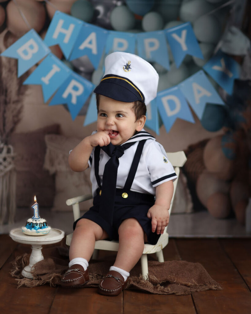 One-year-old boy in a sailor outfit during a nautical-themed first birthday cake smash photography session in Norwood, MA