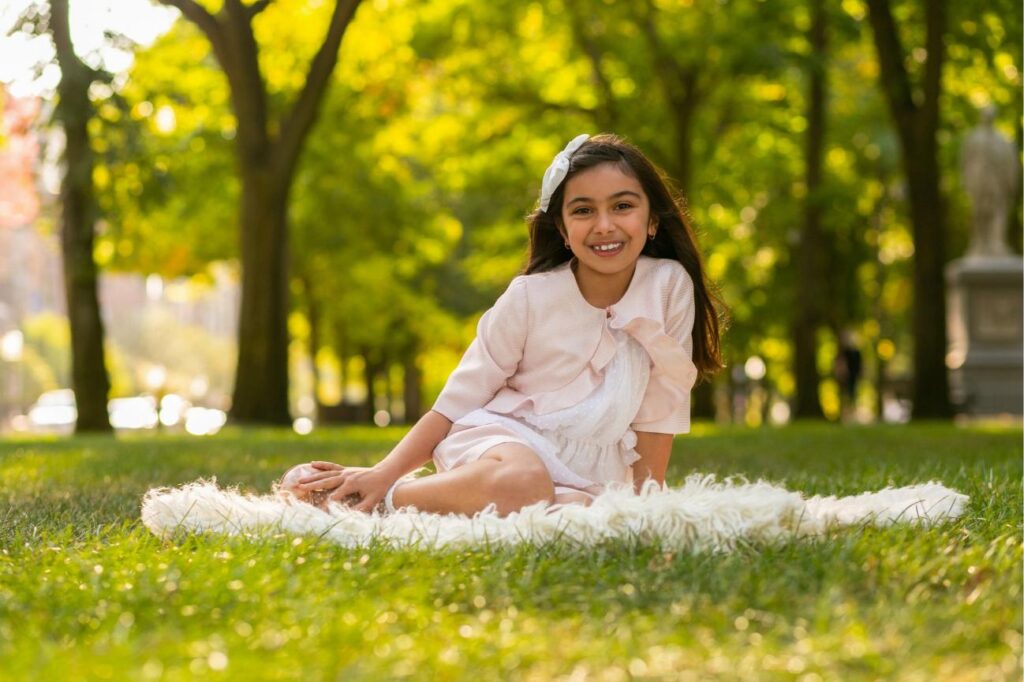 10-year-old girl smiling on a blanket during a natural-light portrait session in the Boston Public Garden