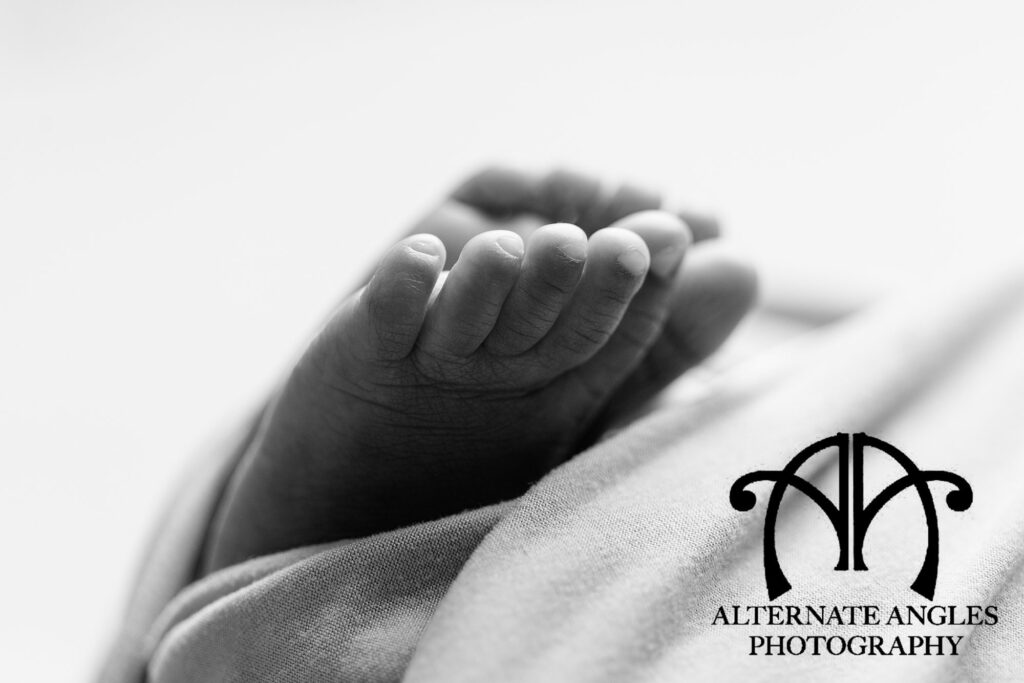 Close-up black-and-white newborn detail photo of a baby’s tiny feet wrapped in a soft blanket