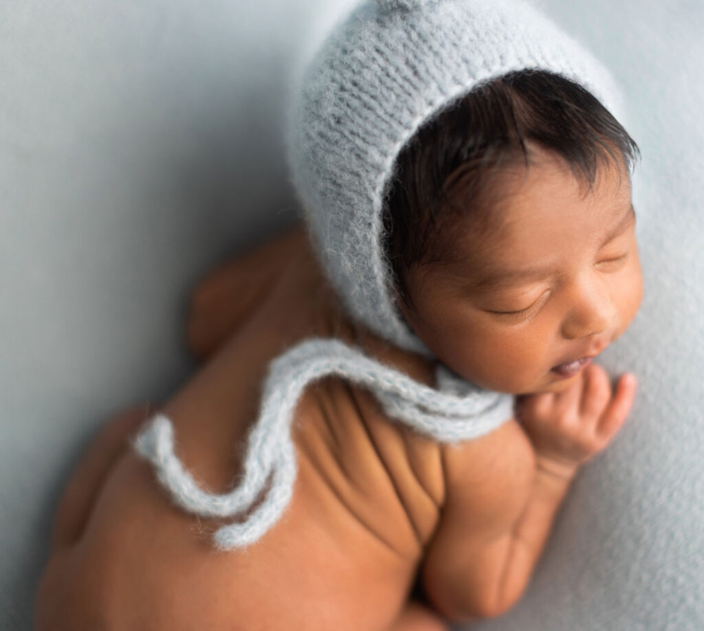 Sleeping newborn baby boy with adorable back wrinkles wearing a knit bonnet during a newborn photography session in Norwood, MA