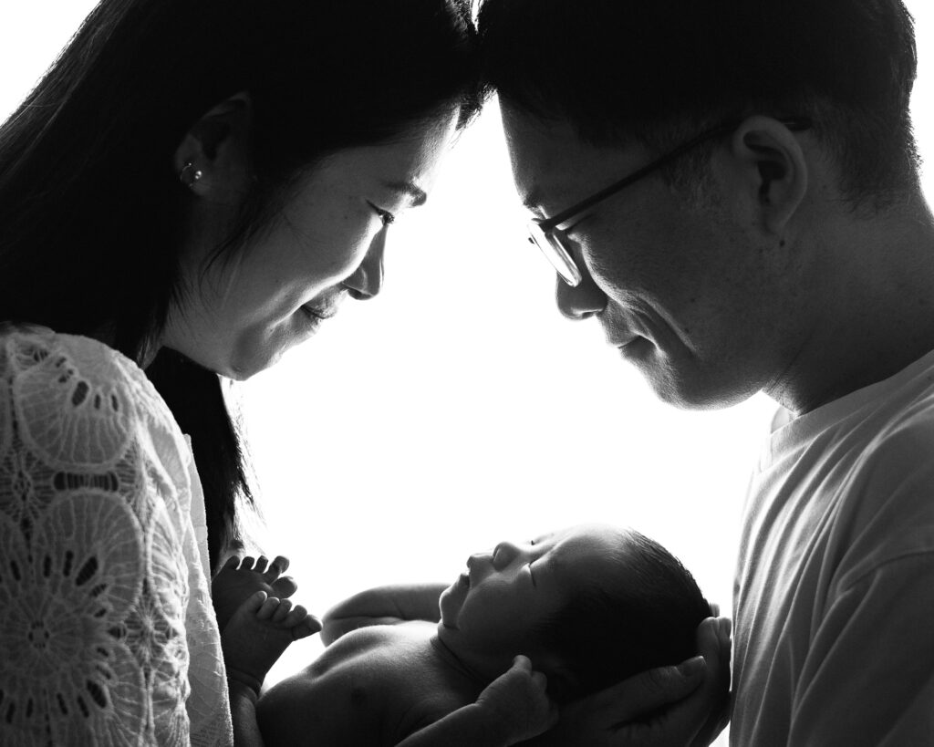 Japanese parents and sibling admiring newborn baby in black-and-white family portrait