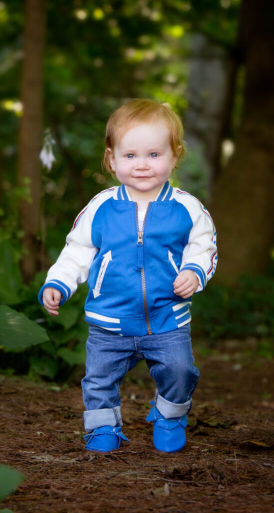 Toddler walking along a woodland path during an outdoor baby milestone photography session in Norwood, MA