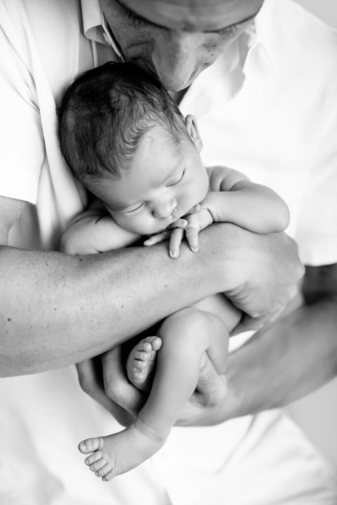 Father holding his sleeping newborn baby in his arms during a black and white newborn photography session