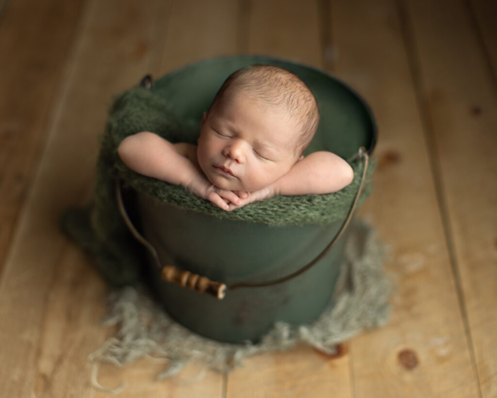 Sleeping newborn boy posed in a green bucket during a Boston newborn photography session