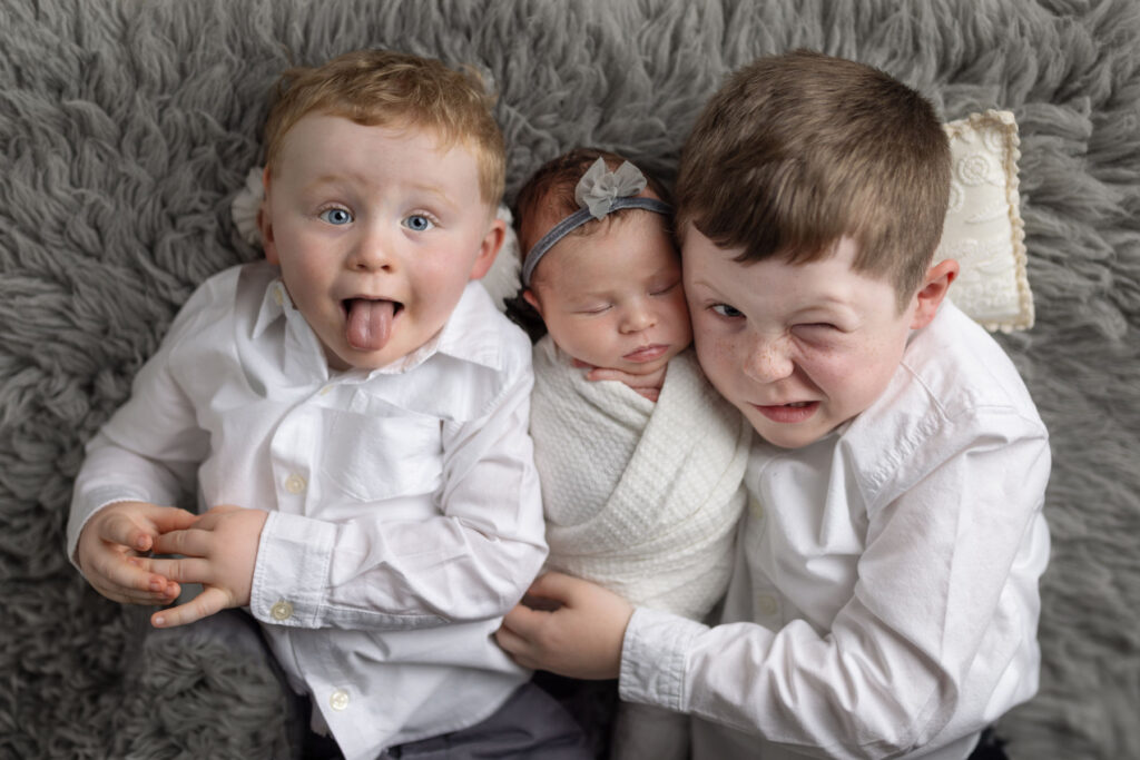 Newborn baby girl with her two older brothers making funny faces during a newborn photography session in Norwood, MA