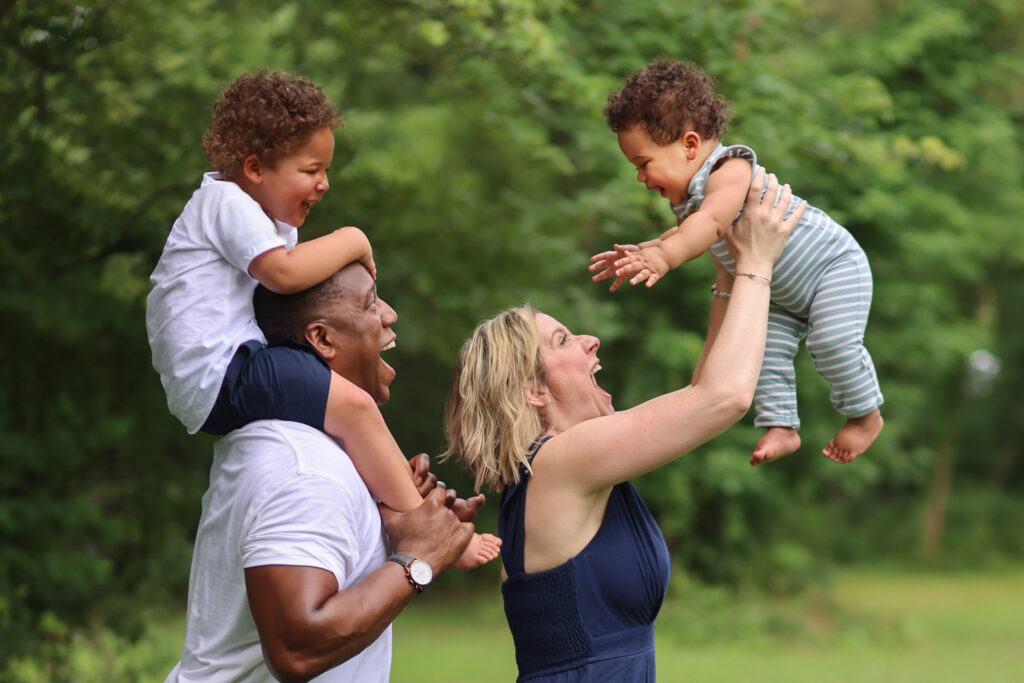 Joyful family portrait with parents playing with their young children during an outdoor session at Alternate Angles Photography in Massachusetts