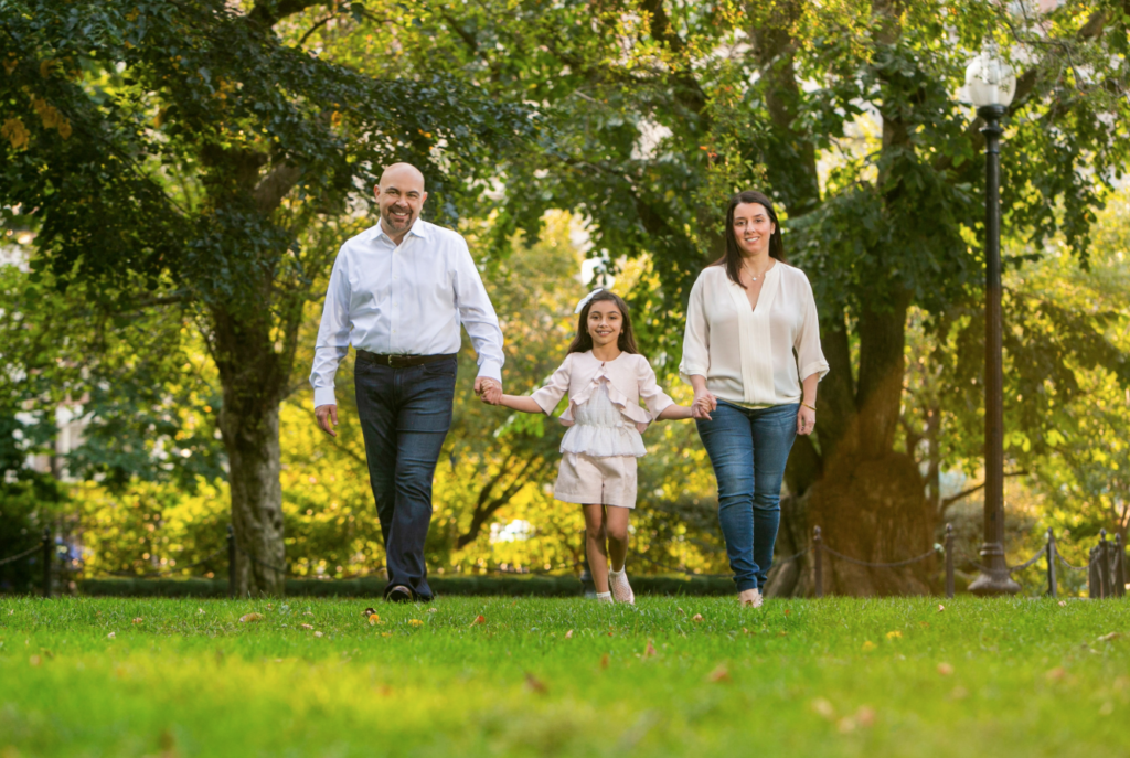 Parents walking hand in hand with their 10-year-old daughter during an outdoor family portrait session in Boston