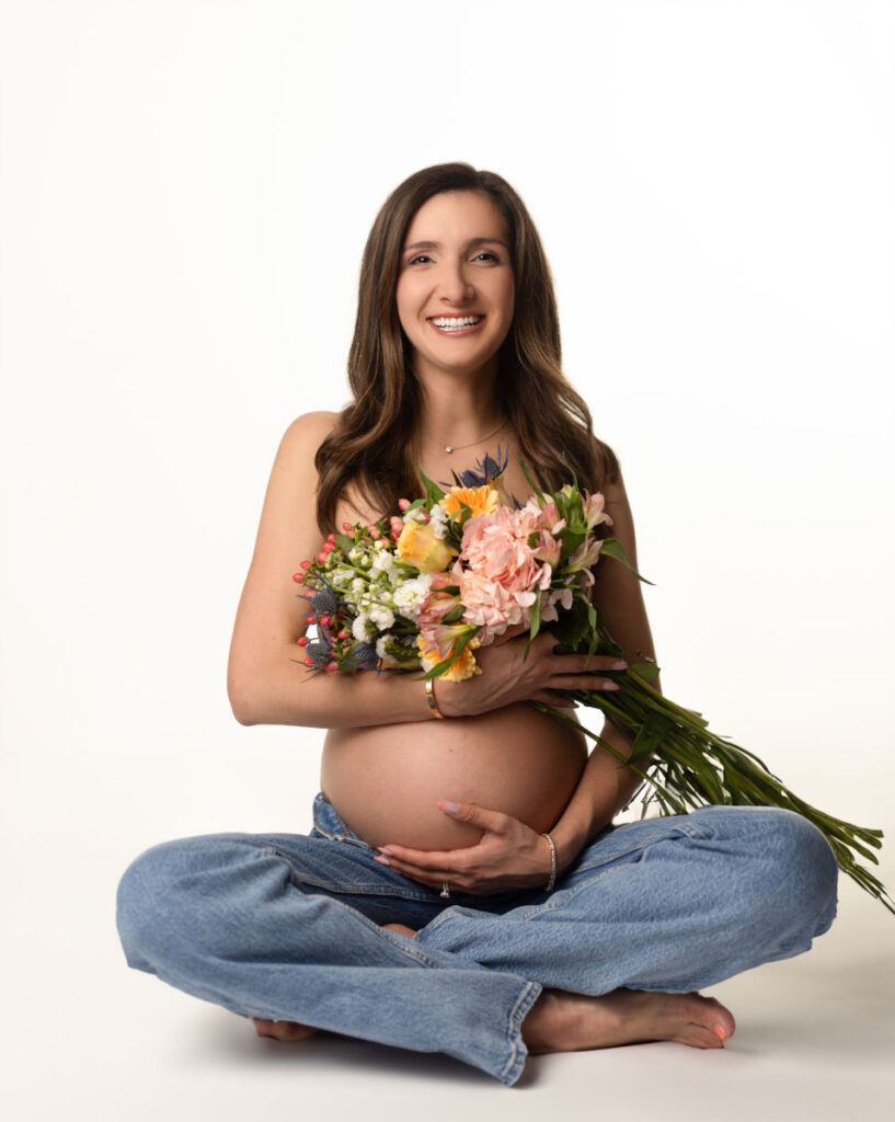 Expectant mother holding a bouquet of flowers during a boho maternity photography session in the Boston area