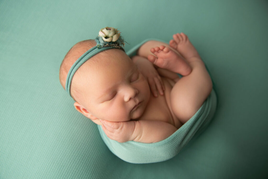 Sleeping newborn baby girl wrapped in sage green fabric during an in-home newborn photography session in Belmont, MA
