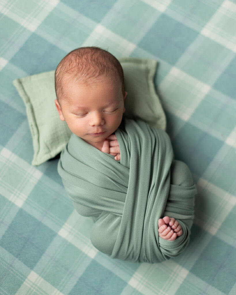 Newborn baby boy wrapped in sage green fabric during a professional newborn photography session in Norwood, MA
