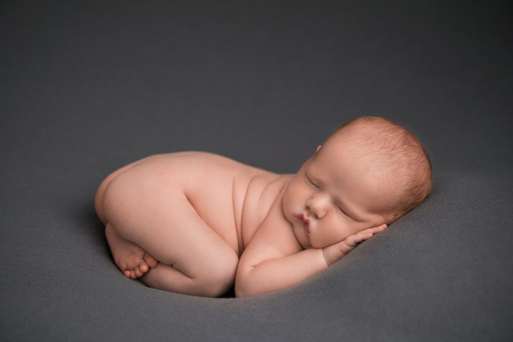 Sleeping newborn baby curled comfortably on a soft charcoal-gray backdrop during a Norwood newborn session.