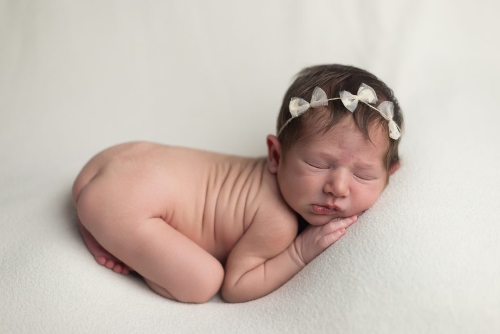 Sleeping newborn baby curled on a cream blanket with a delicate bow headband