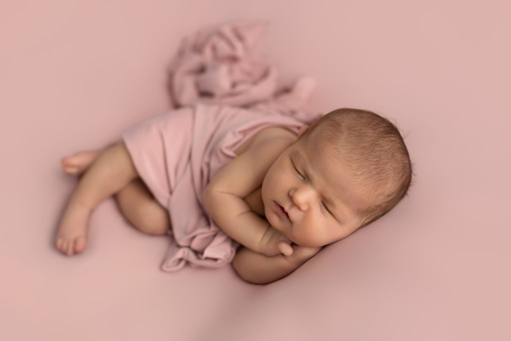 Sleeping newborn baby girl wrapped in blush pink fabric during a professional studio session by a Boston newborn photographer.
