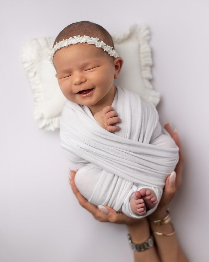 Smiling newborn wrapped securely while being gently supported during a studio newborn photography session.