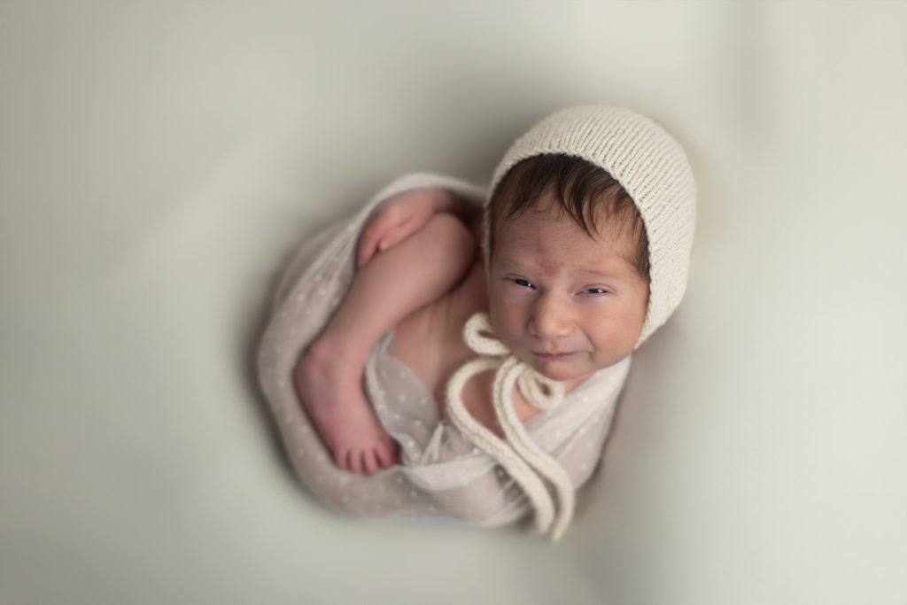 Newborn baby wrapped in cream with a knit bonnet during a Boston newborn photography session