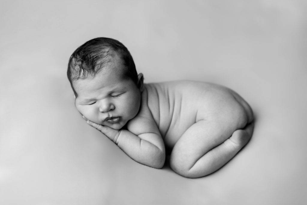 Black and white portrait of a sleeping newborn baby curled into a classic newborn pose.