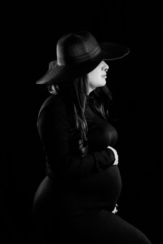 Black and white maternity portrait of an expecting mother wearing a wide-brim hat.