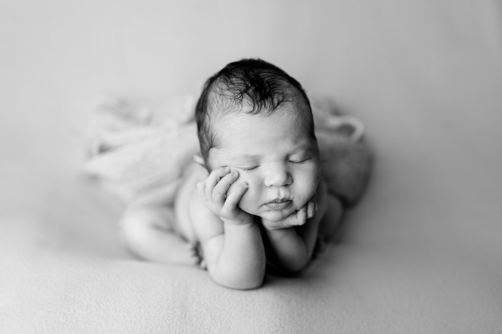 Black and white portrait of a sleeping newborn baby resting her chin in both hands during a professional newborn session.