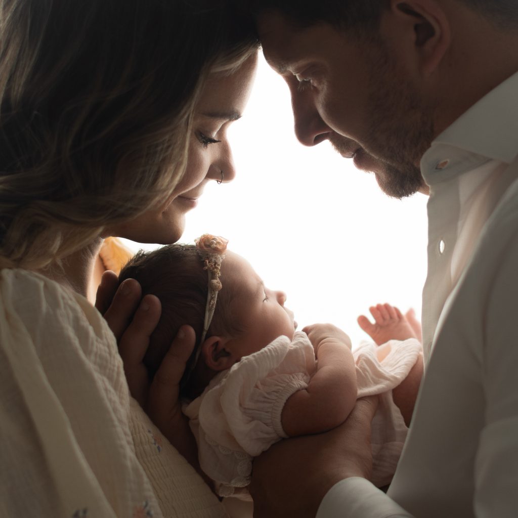 Boston newborn photographer capturing an intimate family portrait of parents lovingly gazing at their newborn baby girl during a studio newborn photography session.