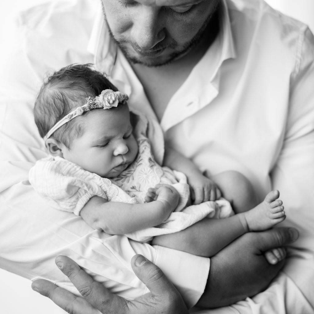 Boston newborn photographer portrait of a father gently holding his sleeping newborn daughter in his arms.