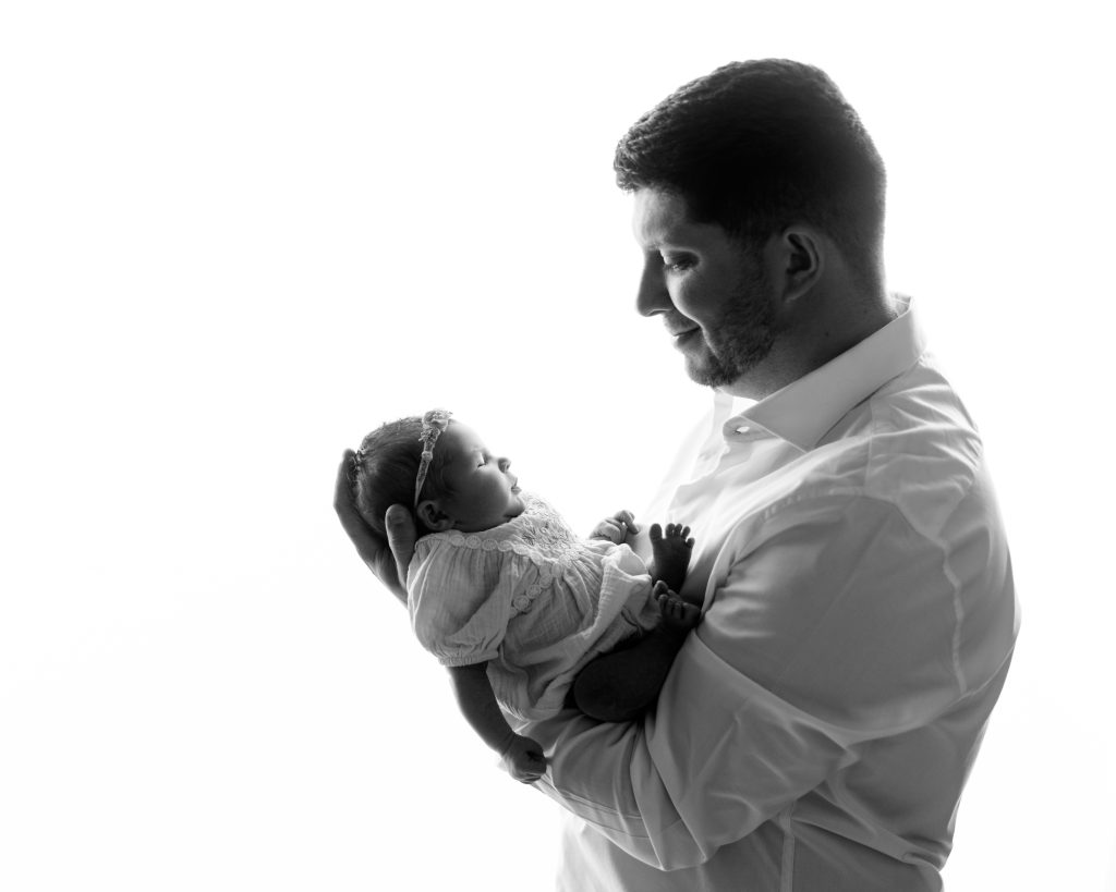 Father lovingly holding his sleeping newborn daughter during a professional newborn photography session in Boston.