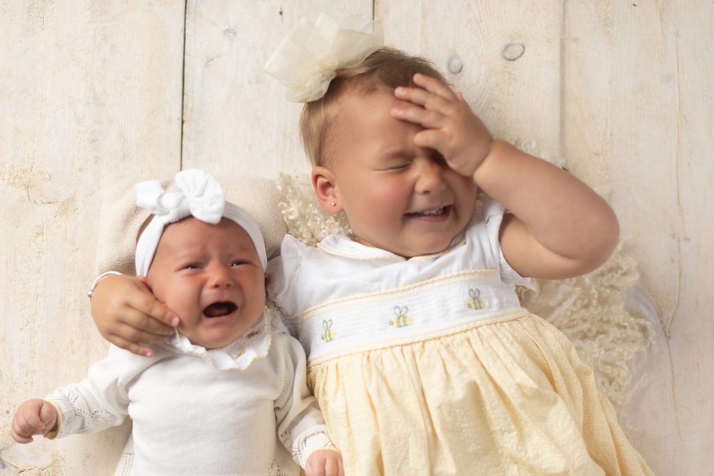Toddler laughing beside a crying newborn during a fun sibling photo taken during a studio newborn photography session in Greater Boston.